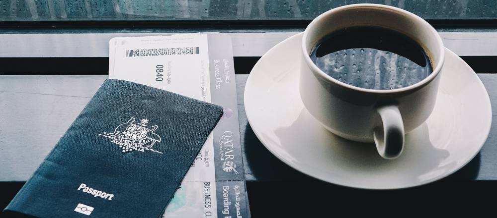 An Australian passport and ticket to move internationally sits on a table next to a coffee