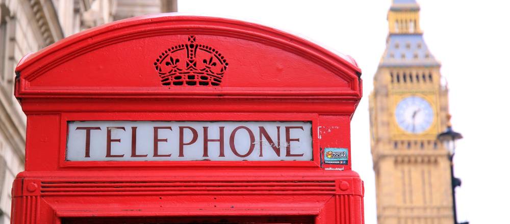 Red London telephone booth with Big Ben in the background.